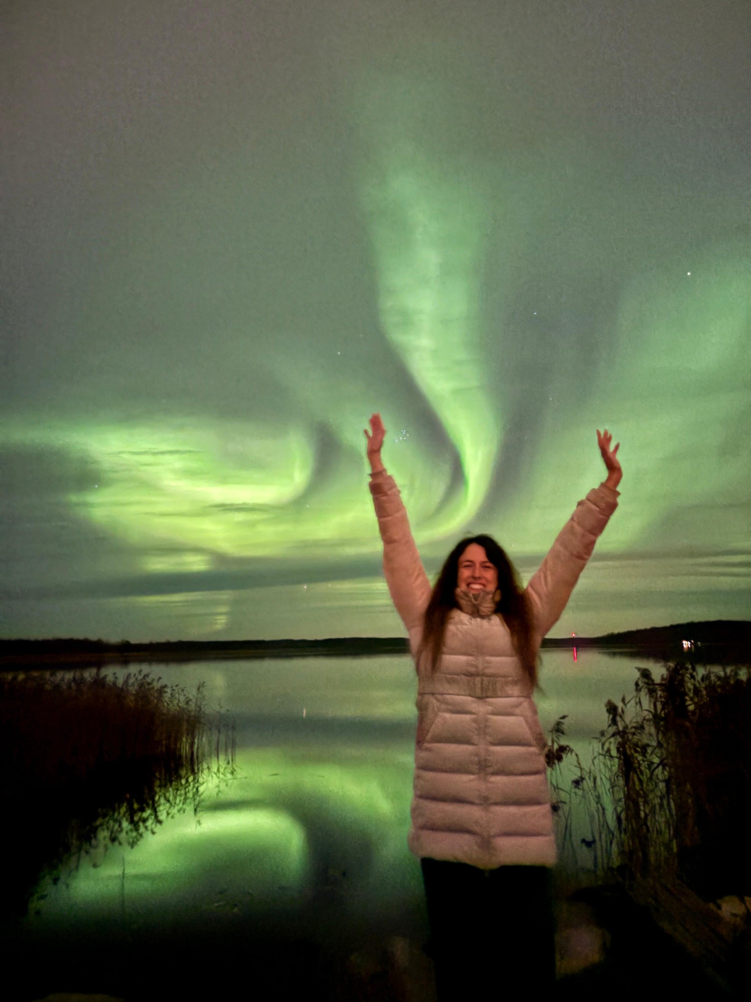 Aurora boreal verde reflejada en un lago de Rovaniemi, con los brazos levantados celebrando la vista
